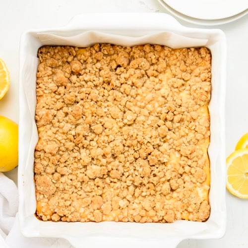 White pan of Lemonade Crumb Bars on a white table with fresh lemon from overhead.