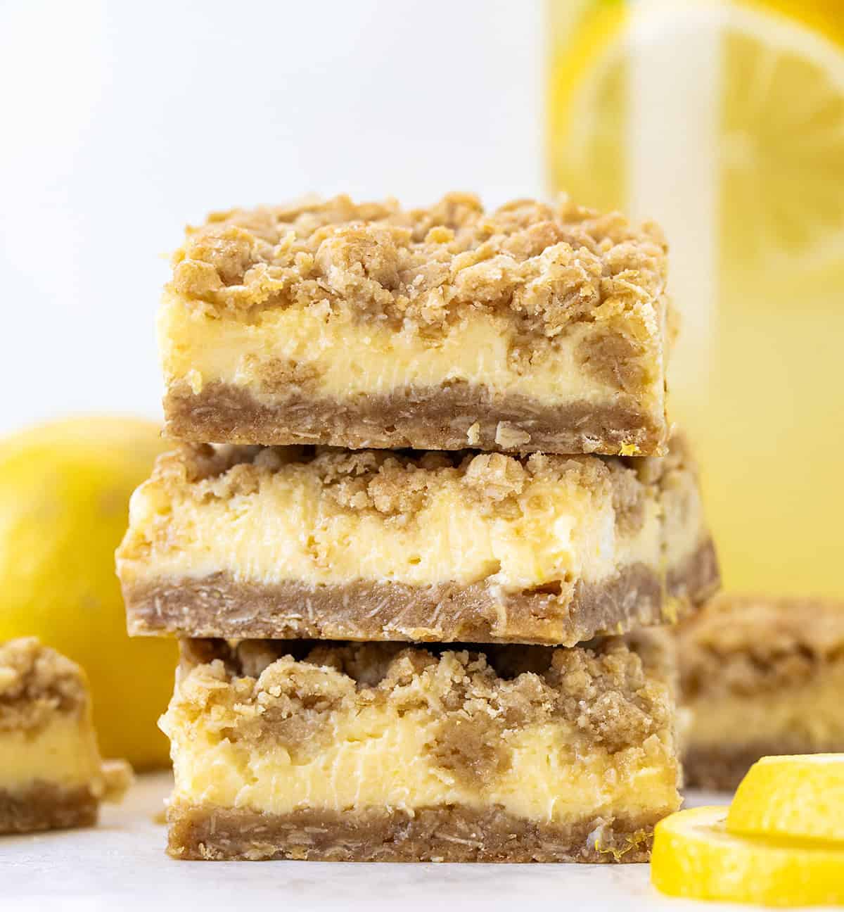 If you love my Lemon Crumb Bars, youโre going to love this fun variation! These Lemonade Crumb Bars use frozen lemonade concentrate for an extra punch of bright, tangy flavor. Theyโre simple to make, with a creamy lemon filling and a soft, crumbly oat crust and topping. Great for summer or anytime youโre craving something sweet and citrusy. Stack of Lemonade Crumb Bars with a pitcher of lemonade in the background.