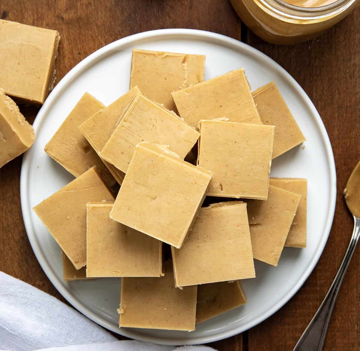This Microwave Peanut Butter Fudge is rich, creamy, and made with just three simple ingredients. It has a smooth, melt-in-your-mouth texture and the perfect sweet-and-salty peanut butter flavor. No stovetop, no candy thermometer--just a microwave and a little chill time! White platter of Microwave Peanut Butter Fudge on a wooden table from overhead.