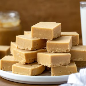 Microwave Peanut Butter Fudge cut into squares and stacked on a white platter on a wooden table.