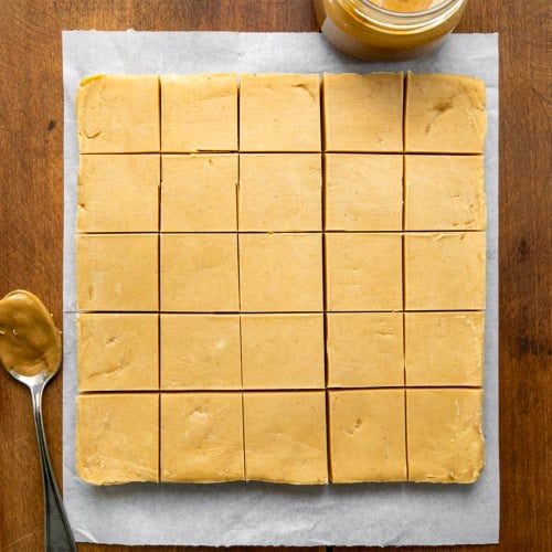 Microwave Peanut Butter Fudge cut into squares on a piece of parchment paper on a wooden table from overhead.