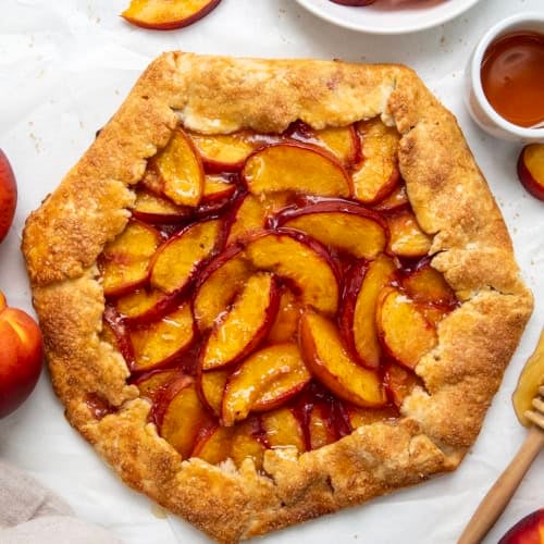 Peach Galette on a white table with fresh peaches from overhead.