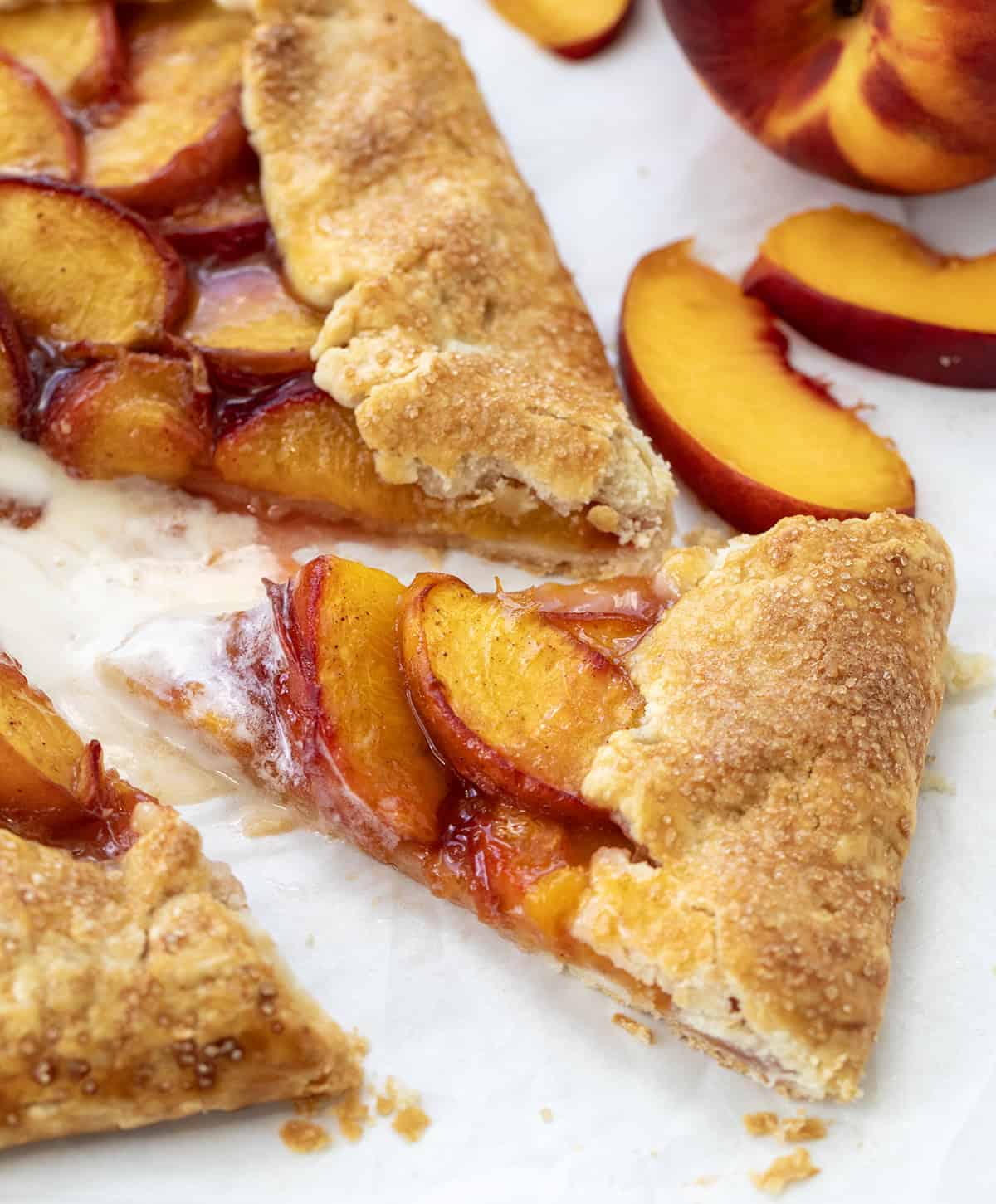 This easy Peach Galette is the perfect summer dessert, made with juicy, fresh peaches wrapped in a buttery, flaky pie crust and baked until golden and bubbling. It is simpler than pie, made with ingredients you probably already have on hand, but just as delicious! Slice of Peach Galette cut near the galette with fresh peaches.