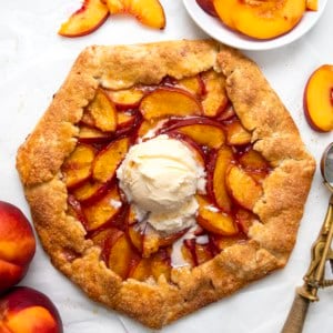 Peach Galette with vanilla ice cream on a white table with fresh peaches.
