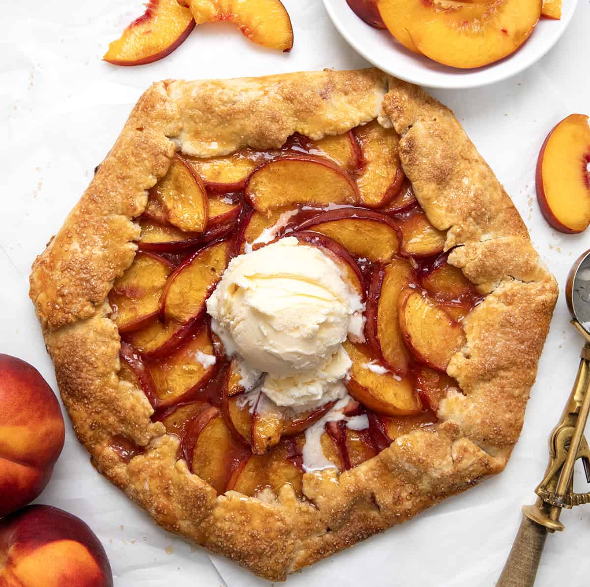 Peach Galette with vanilla ice cream on a white table with fresh peaches.