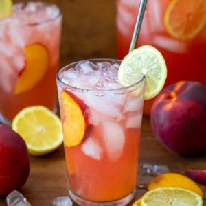 Glasses of Peach Lemonade on a wooden table with fresh lemons and peaches all around.