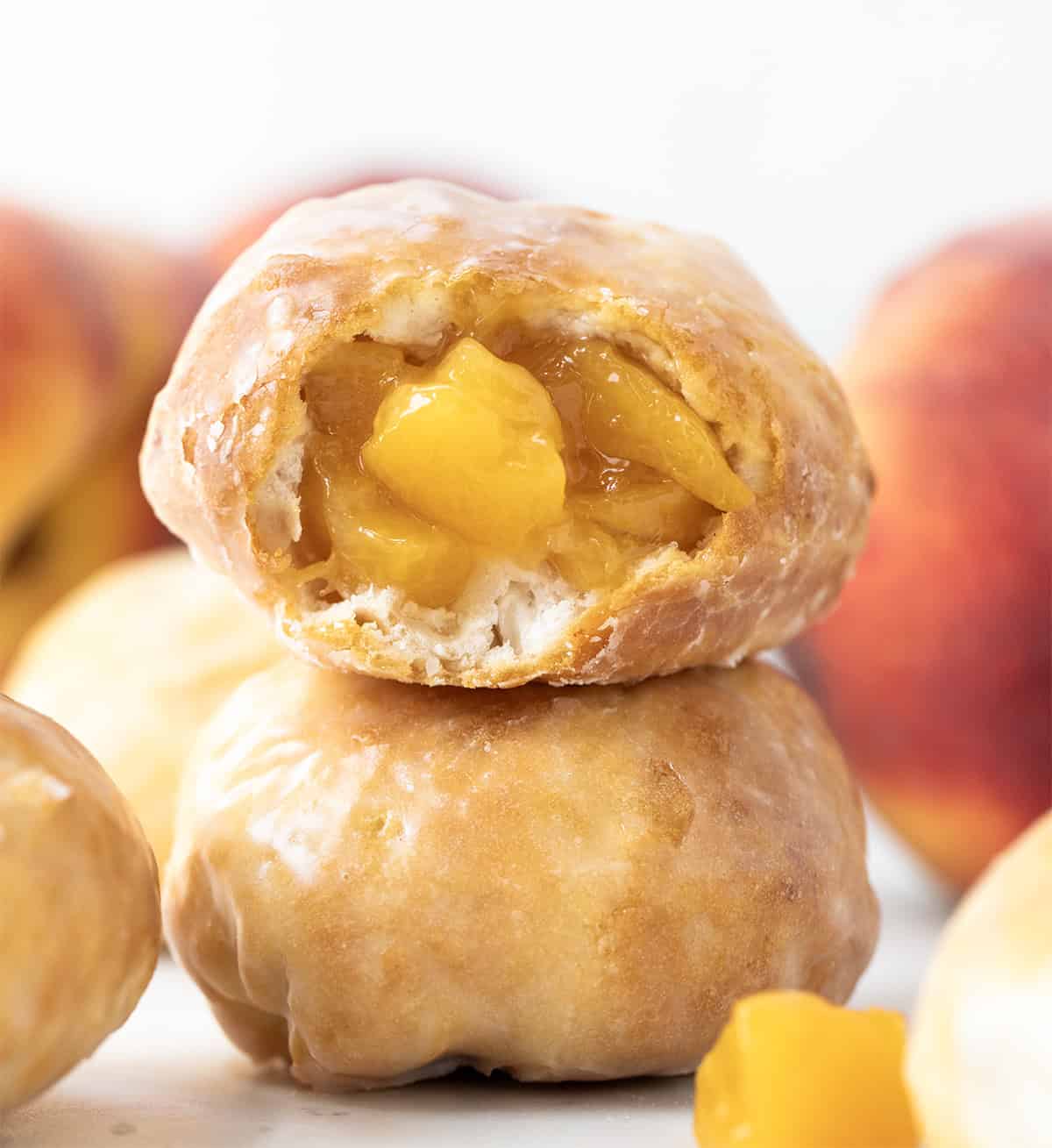 Peach Pie Bombs stacked on a white table with top peach pie bomb bit into showing peaches inside.