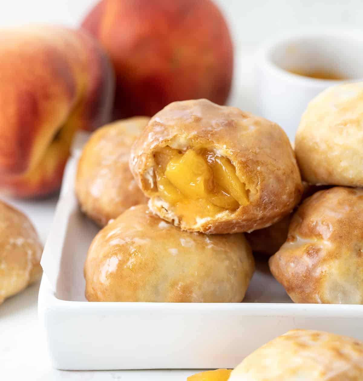 Peach Pie Bombs in a white platter with one bomb bit into showing inside peaches.