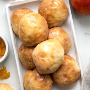 White platter of Peach Pie Bombs on a white table with fresh peaches from overhead.