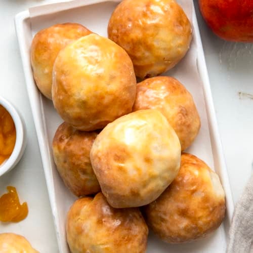 White platter of Peach Pie Bombs on a white table with fresh peaches from overhead.