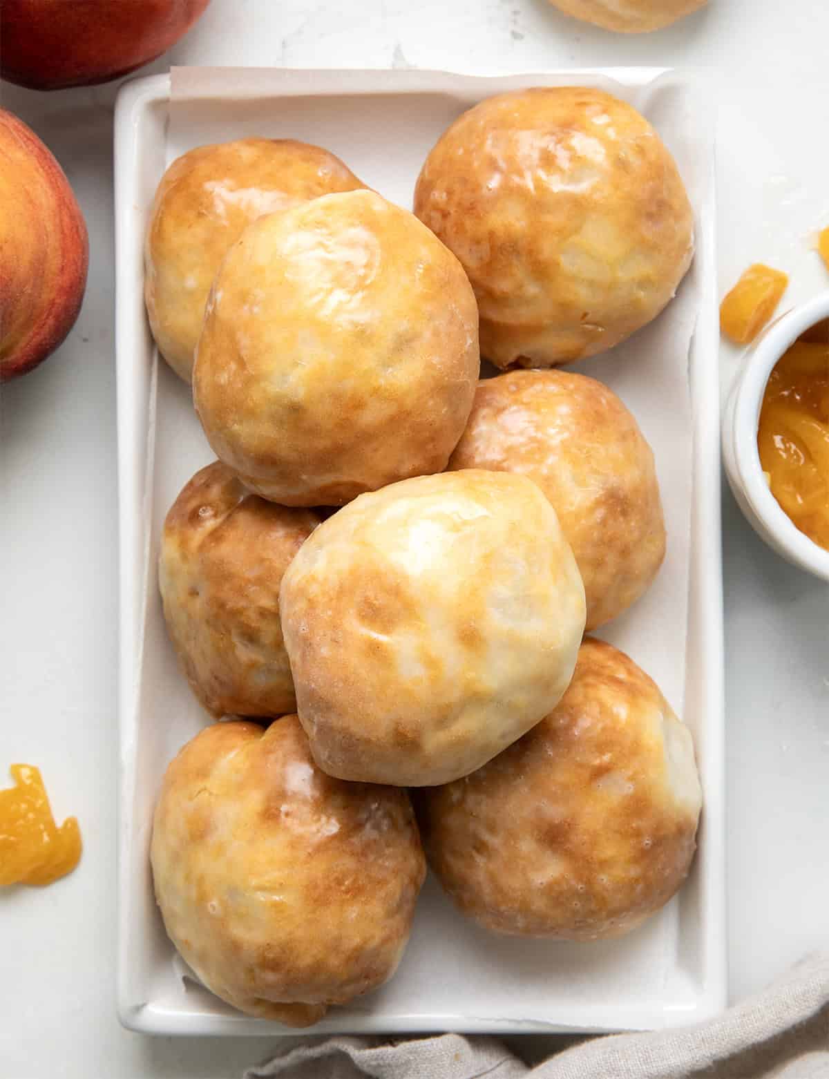 White platter of Peach Pie Bombs on a white table with fresh peaches from overhead.