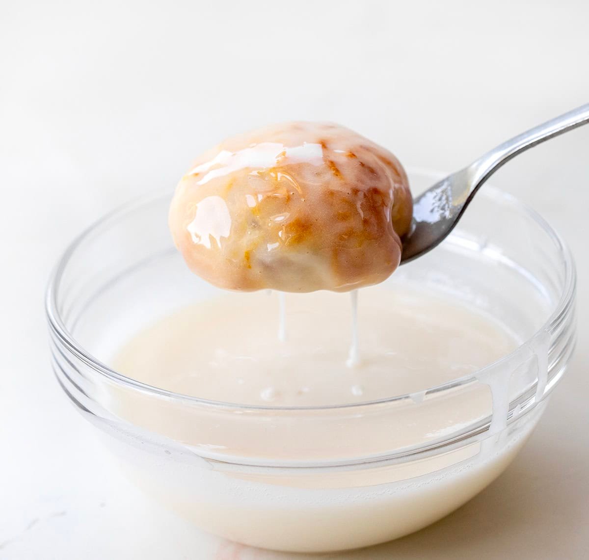 Dipping Peach Pie Bomb into glaze with a fork.