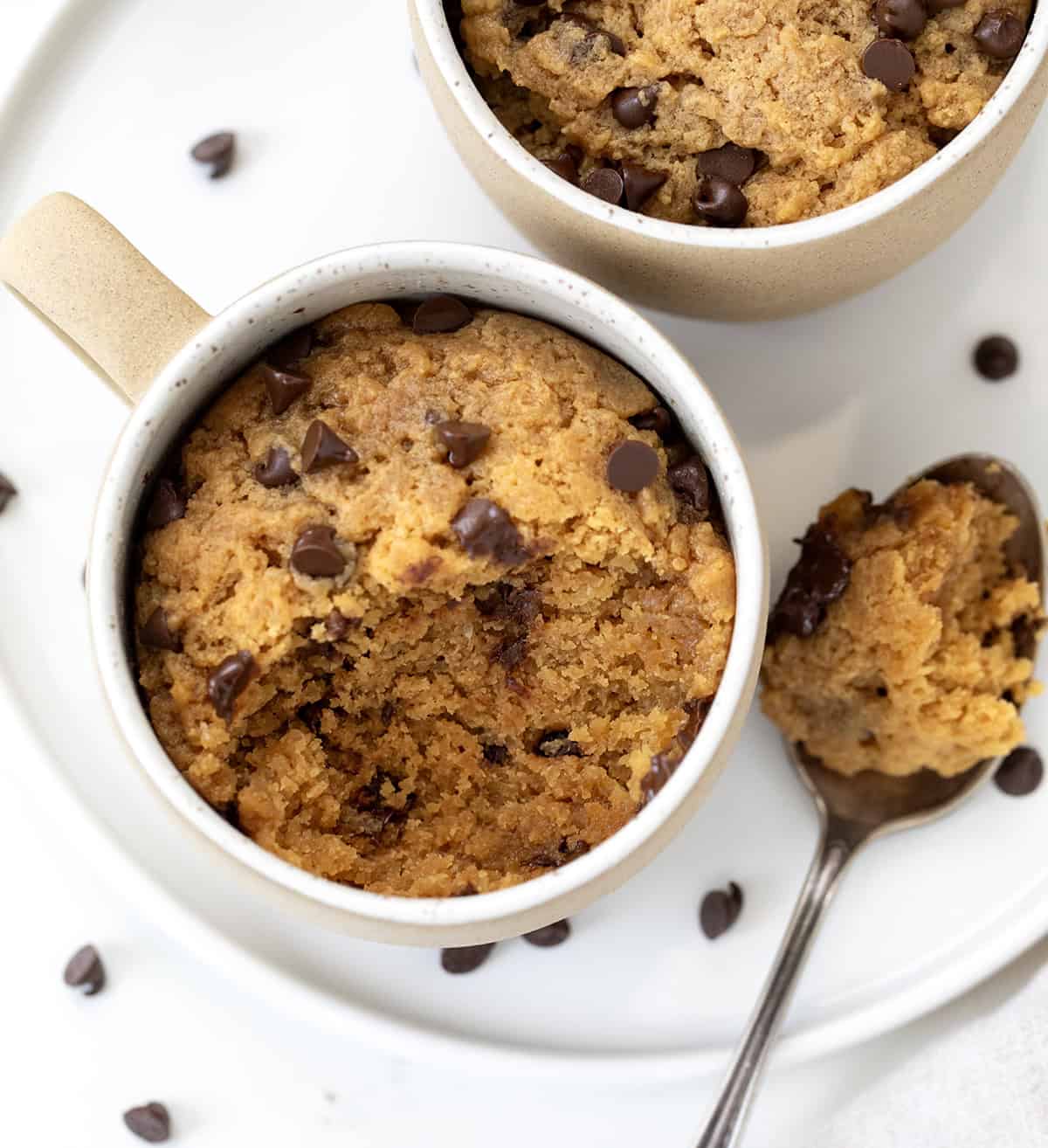 This microwave Peanut Butter Mug Cake is rich, gooey, and ready in just minutes, no oven needed! It's a quick and satisfying single-serve dessert for peanut butter lovers. I love that I can satisfy a sweet craving without baking a whole cake! Mugs of Peanut Butter cake with a portion removed from one mug shot from overhead.