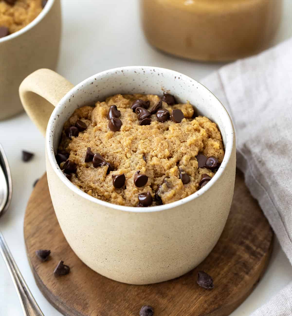 This microwave Peanut Butter Mug Cake is rich, gooey, and ready in just minutes, no oven needed! It's a quick and satisfying single-serve dessert for peanut butter lovers. I love that I can satisfy a sweet craving without baking a whole cake! Peanut Butter Mug Cakes on a white table with mini chocolate chips.