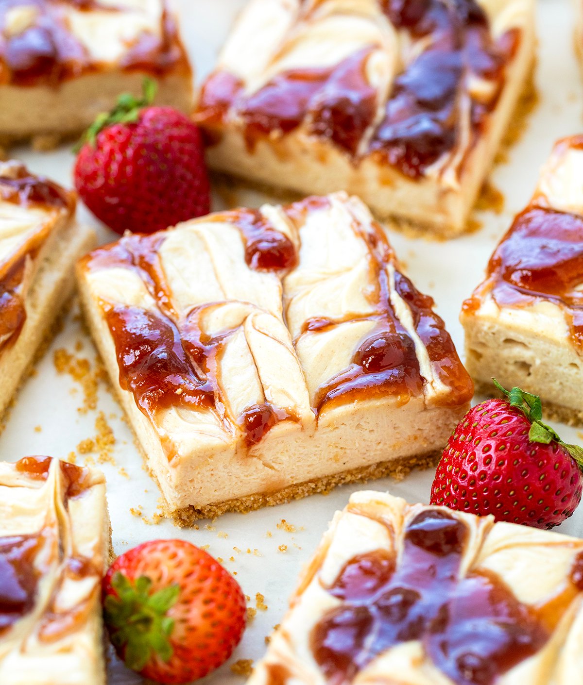 Peanut Butter and Jelly Cheesecake Bars on a white table with fresh strawberries.