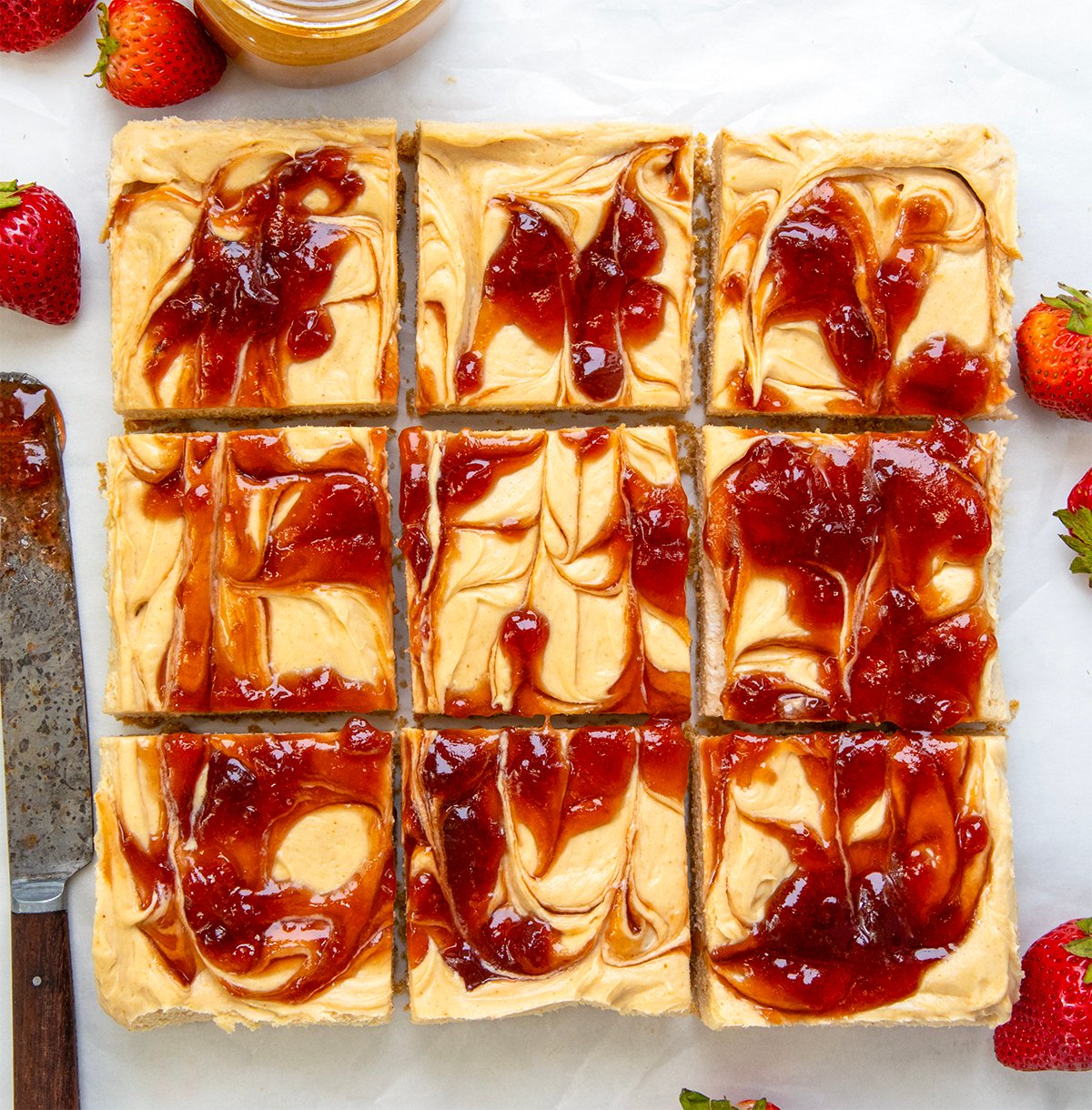 Peanut Butter and Jelly Cheesecake Bars cut into squares on a white table from overhead.