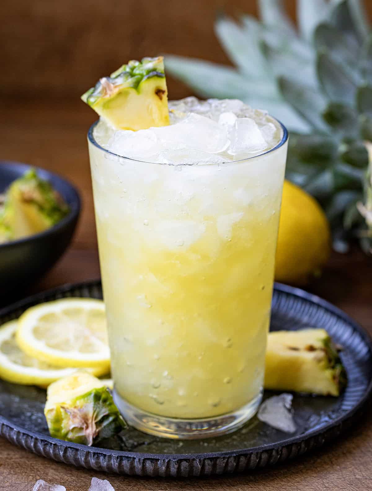 Glass of Pineapple Bourbon Fizz on a tray with freshly sliced lemons.