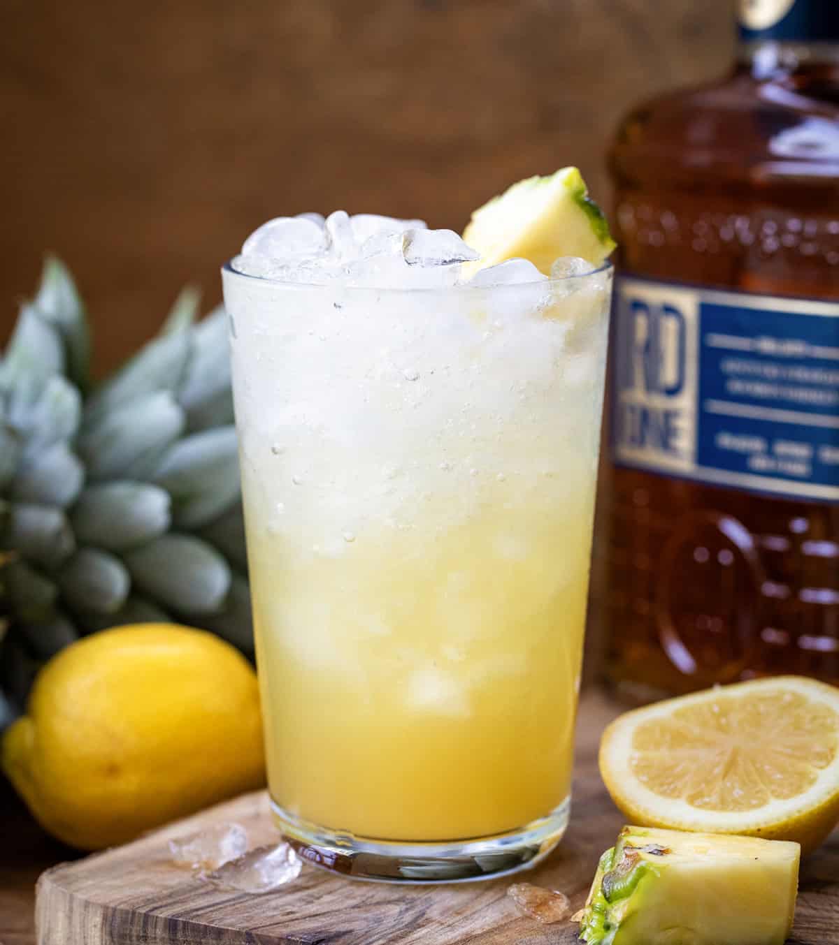 Glass of Pineapple Bourbon Fizz on a cutting board with freshly sliced lemons.