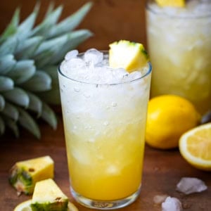 Glass of Pineapple Bourbon Fizz on a wooden table with freshly sliced lemons.
