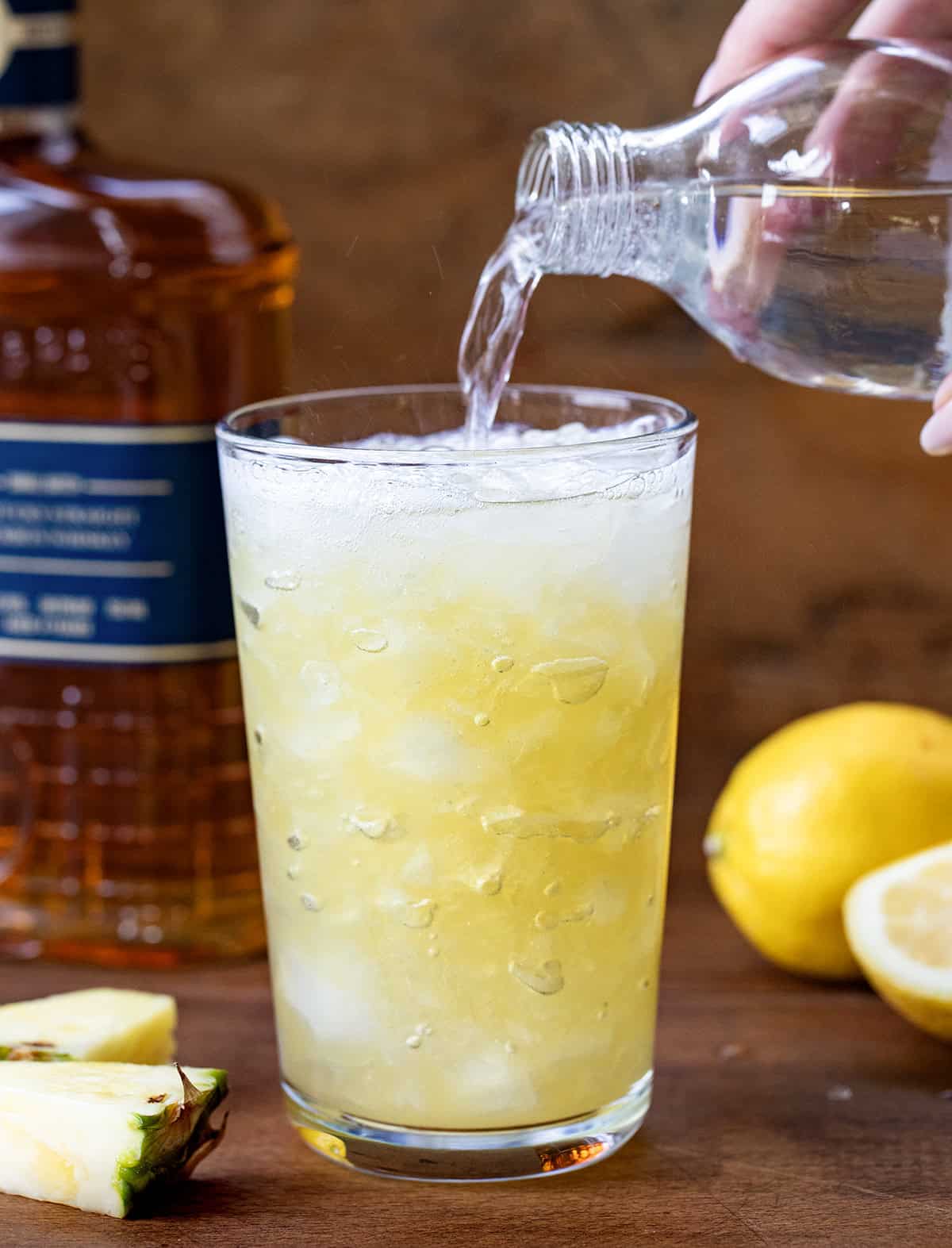 Pouring soda into a Pineapple Bourbon Fizz.