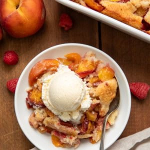 White plate with Raspberry Peach Cobbler on it and a scoop of ice cream and fresh peaches from overhead.
