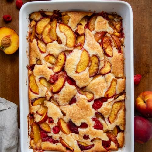 White pan of Raspberry Peach Cobbler on a wooden table from overhead.