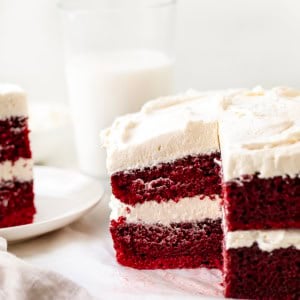Cut into Sheet Pan Red Velvet Cake with a slice on a plate and glasses of milk in the background.