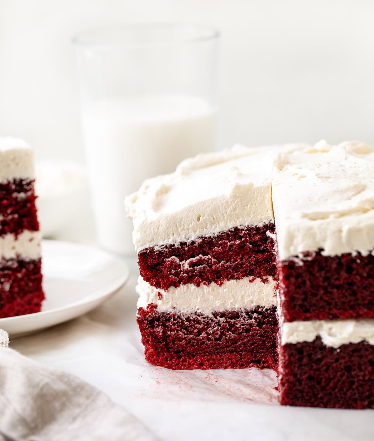 If you love red velvet, this Sheet Pan Red Velvet Cake is the easy, crowd-friendly dessert you’ve been looking for. It’s soft, moist, and full of that classic cocoa-vanilla flavor. The cake is layered with silky ermine frosting for a beautiful stacked presentation that feels extra special, without the stress of baking two separate layers! Cut into Sheet Pan Red Velvet Cake with a slice on a plate and glasses of milk in the background.