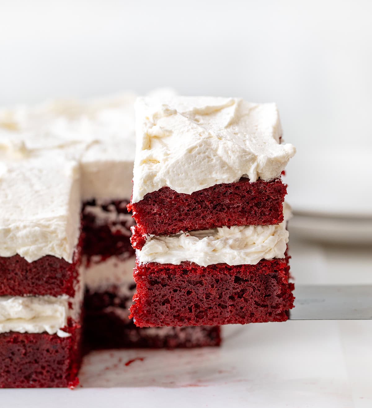 If you love red velvet, this Sheet Pan Red Velvet Cake is the easy, crowd-friendly dessert you’ve been looking for. It’s soft, moist, and full of that classic cocoa-vanilla flavor. The cake is layered with silky ermine frosting for a beautiful stacked presentation that feels extra special, without the stress of baking two separate layers! Spatula picking up a slice of Sheet Pan Red Velvet Cake.