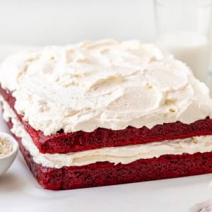 Sheet Pan Red Velvet Cake on a white table with ermine frosting and glasses of milk.