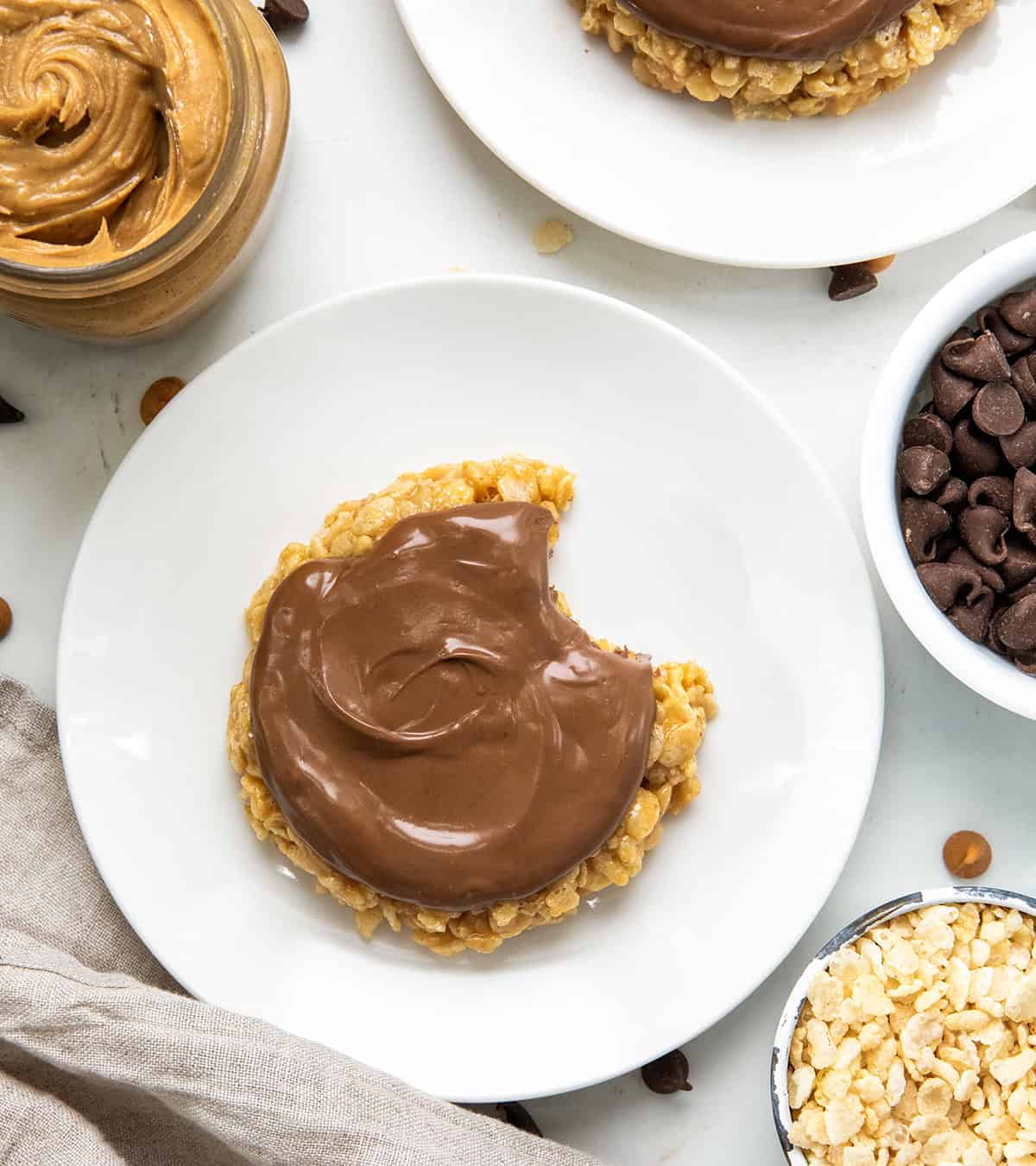 This One-Minute Scotcheroo (made in a mug) is my go-to when I’m craving something sweet and quick, just for me! All the classic Scotcheroo flavor, shaped like a cookie, no oven needed! Single-Serving Scotcheroo's on white plates and one has a bite taken out of it.