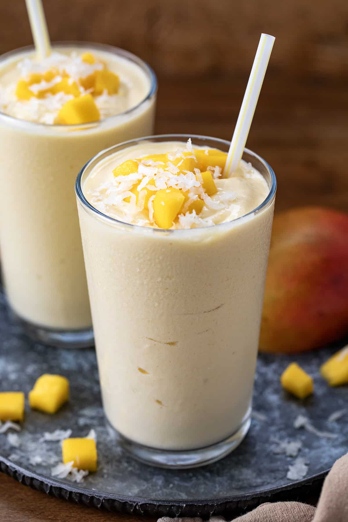 Two Tropical Mango Milkshakes on a wooden table with fresh mango and coconut.