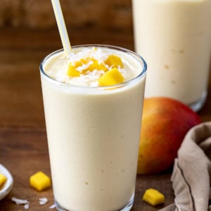 Two Tropical Mango Milkshakes on a wooden table with fresh mango and coconut.