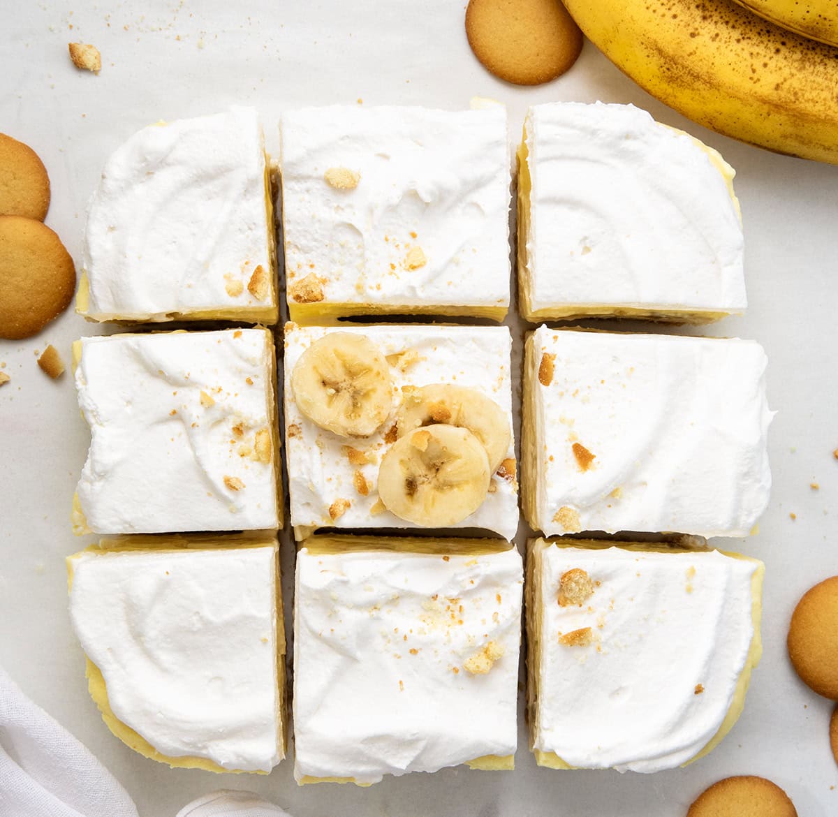 These Banana Cream Bars are an easy summer dessert that everyone will love! The no-bake dessert has a vanilla wafer crust, creamy filling, fresh bananas, and fluffy topping. Itโs cool, creamy, and perfect for hot days when you donโt want to turn on the oven. Banana Cream Pie Bars cut into squares from overhead with vanilla wafers and fresh banans.