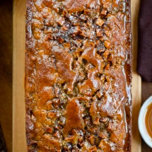 Caramel Apple Fritter Bread on a cutting board on a wooden table with caramel and apples from overhead.