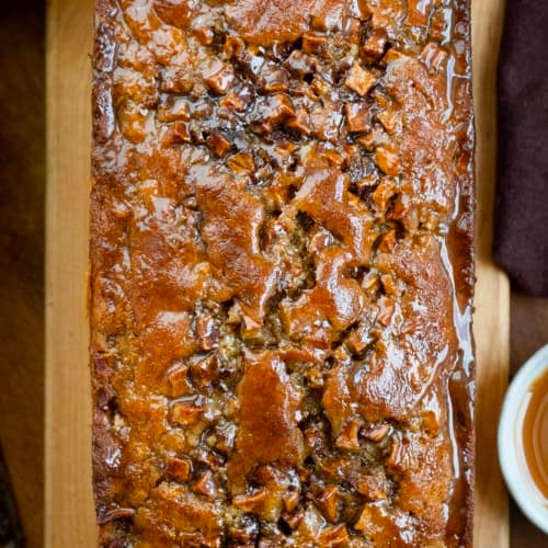 Caramel Apple Fritter Bread on a cutting board on a wooden table with caramel and apples from overhead.