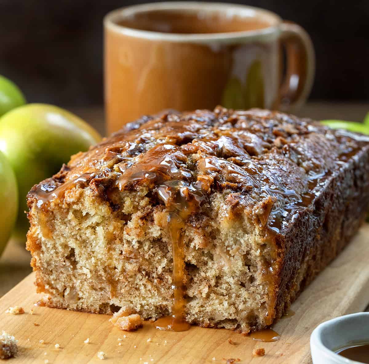 Caramel Apple Fritter Bread takes my fan-favorite Apple Fritter Bread and layers in a sweet caramel drizzle for the ultimate fall baking treat. Soft and tender with cinnamon-sugar apples swirled throughout, this bread is like biting into a caramel apple fritter, with no frying required! Loaf of Caramel Apple Fritter Bread with a piece removed on a wooden table.