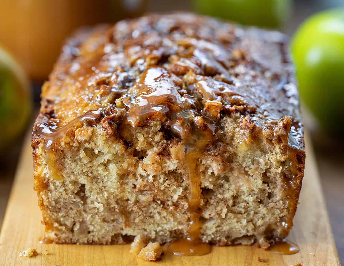 Caramel Apple Fritter Bread takes my fan-favorite Apple Fritter Bread and layers in a sweet caramel drizzle for the ultimate fall baking treat. Soft and tender with cinnamon-sugar apples swirled throughout, this bread is like biting into a caramel apple fritter, with no frying required! Close up of Caramel Apple Fritter Bread on a cutting board with caramel drizzled off the bread.