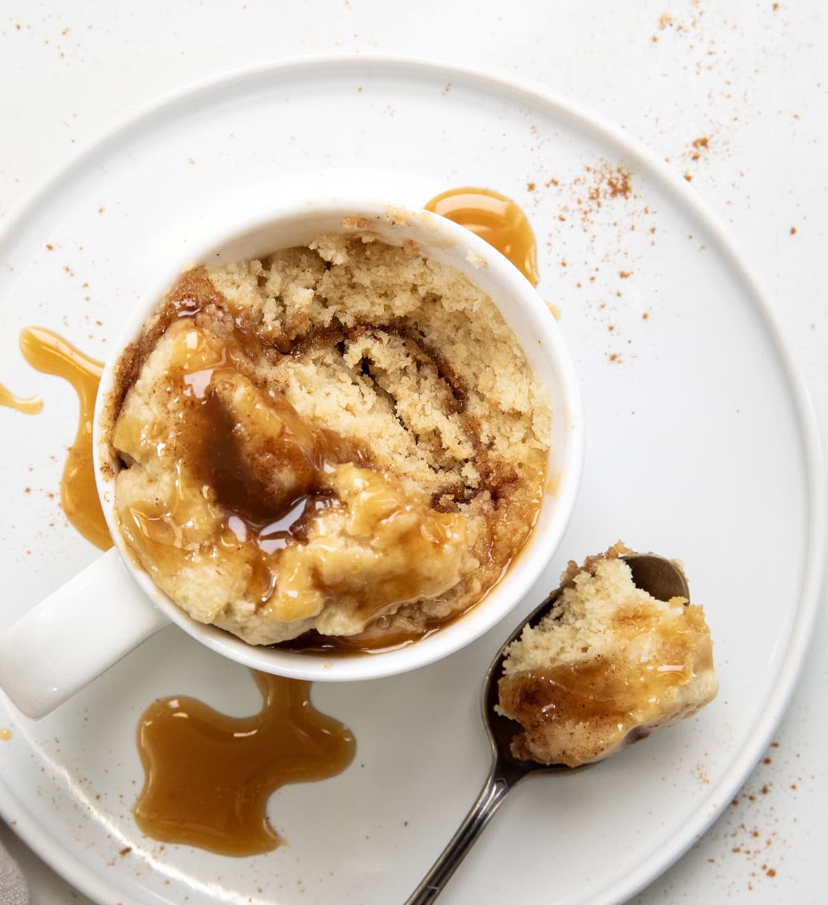 Looking down into a mug of caramel roll with a spoon next to the mug.