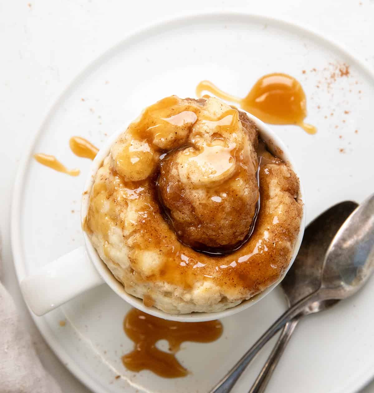 Caramel Roll Mug Cake on a white plate on a white table from overhead.