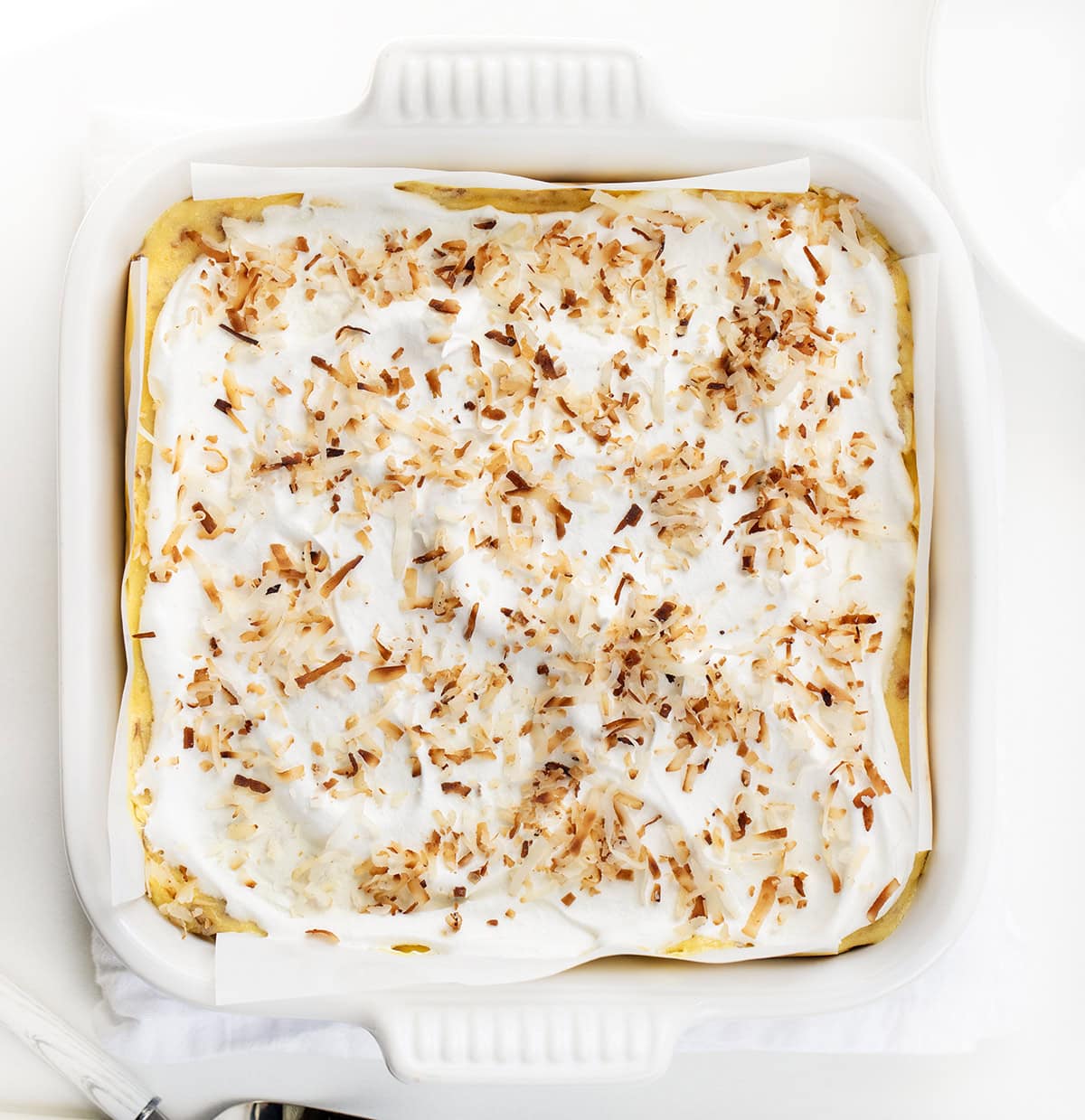 Creamy Coconut Cream Pie Bars with a buttery baked crust, smooth cream cheese layer, and fluffy coconut pudding topped with whipped cream and toasted coconut. Perfect, easy dessert for any occasion! Coconut Cream Pie Bars in a white pan on a white table from overhead.