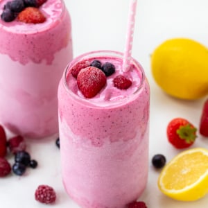 Glasses of Frosted Mixed Berry Lemonade on a white table with fresh and frozen fruit.