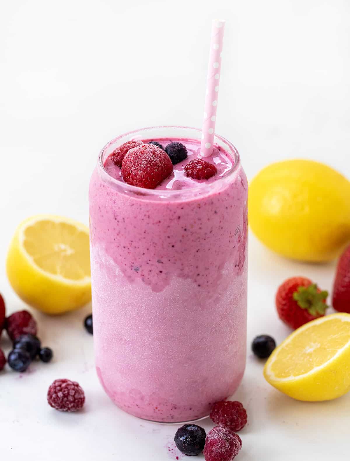 Glass of Frosted Mixed Berry Lemonade on a white table with fresh and frozen fruit.