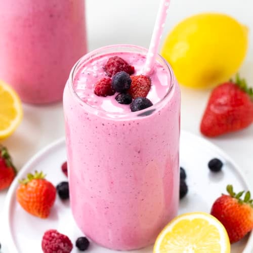 Glass of Frosted Mixed Berry Lemonade on a white plate with fresh and frozen fruit.