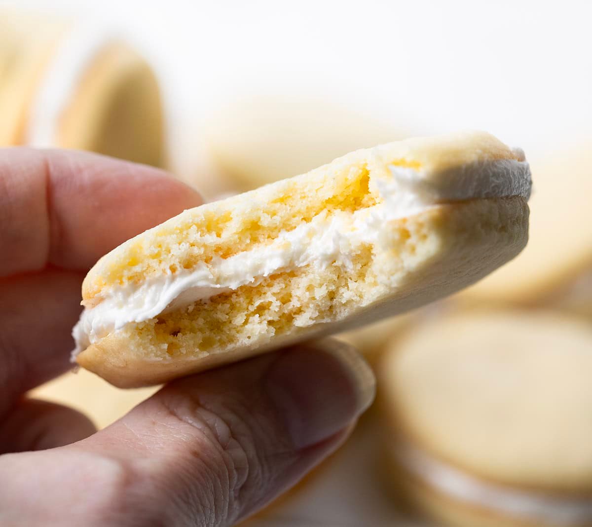 If you love Golden Oreos, you have to try these homemade Golden Oreo cookies! Theyโre soft, buttery sandwich cookies filled with my creamy marshmallow buttercream for the perfect sweet bite! Hand holding a bite into a homemade Golden Oreo Cookie.