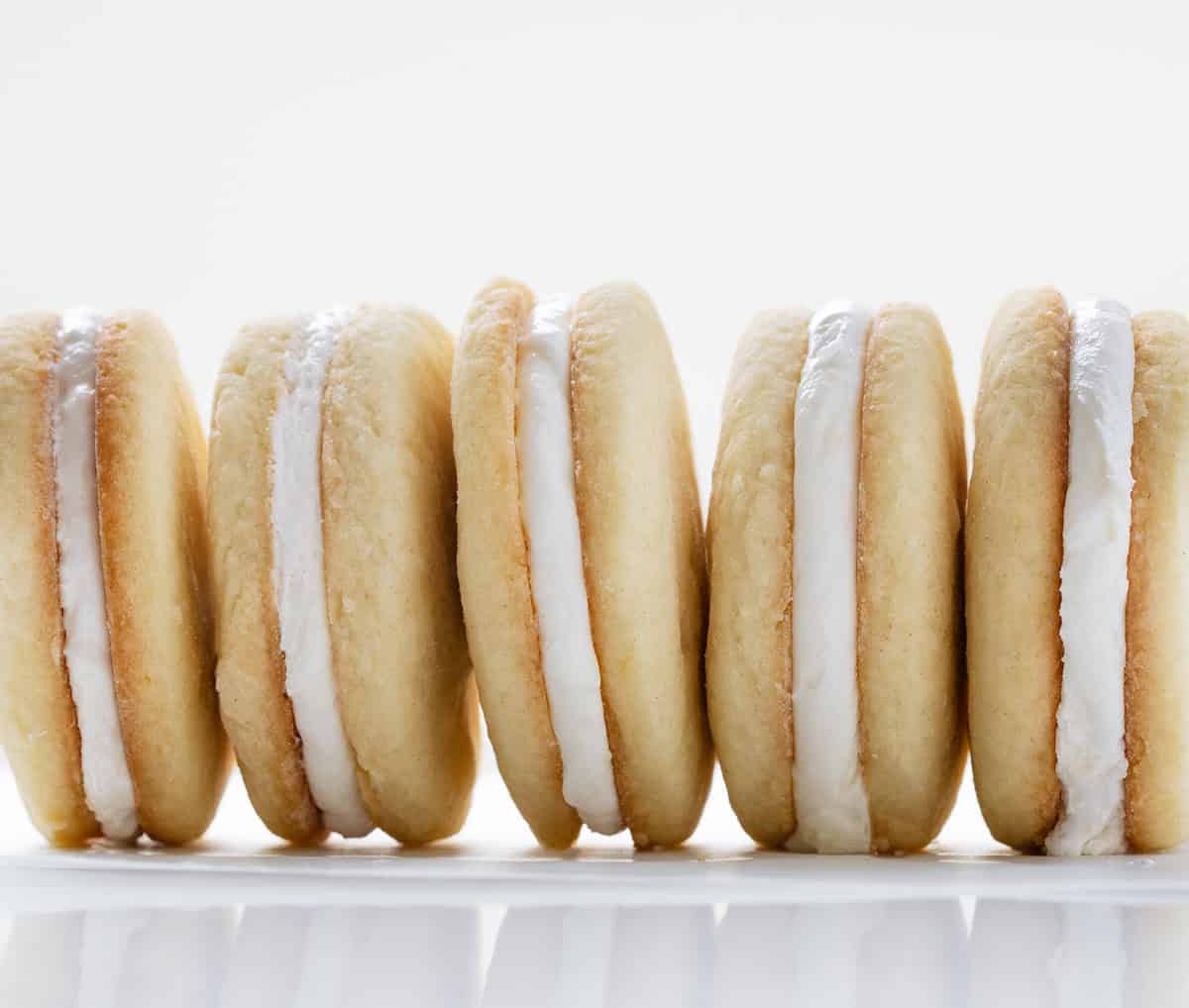 If you love Golden Oreos, you have to try these homemade Golden Oreo cookies! Theyโre soft, buttery sandwich cookies filled with my creamy marshmallow buttercream for the perfect sweet bite! Homemade Golden Oreo Cookies stacked on their sides on a white table very close up.