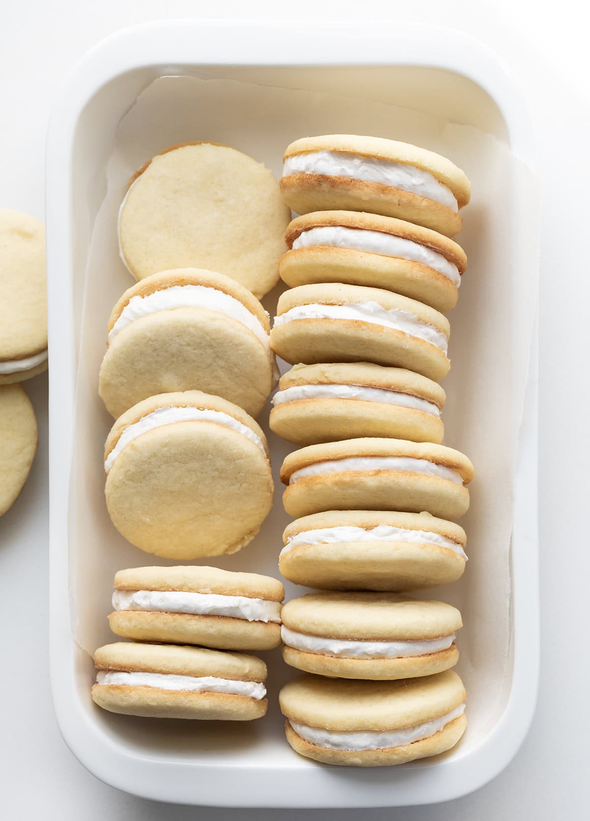 If you love Golden Oreos, you have to try these homemade Golden Oreo cookies! Theyโre soft, buttery sandwich cookies filled with my creamy marshmallow buttercream for the perfect sweet bite! Small white platter of Golden Oreo Cookies on a white table from overhead.