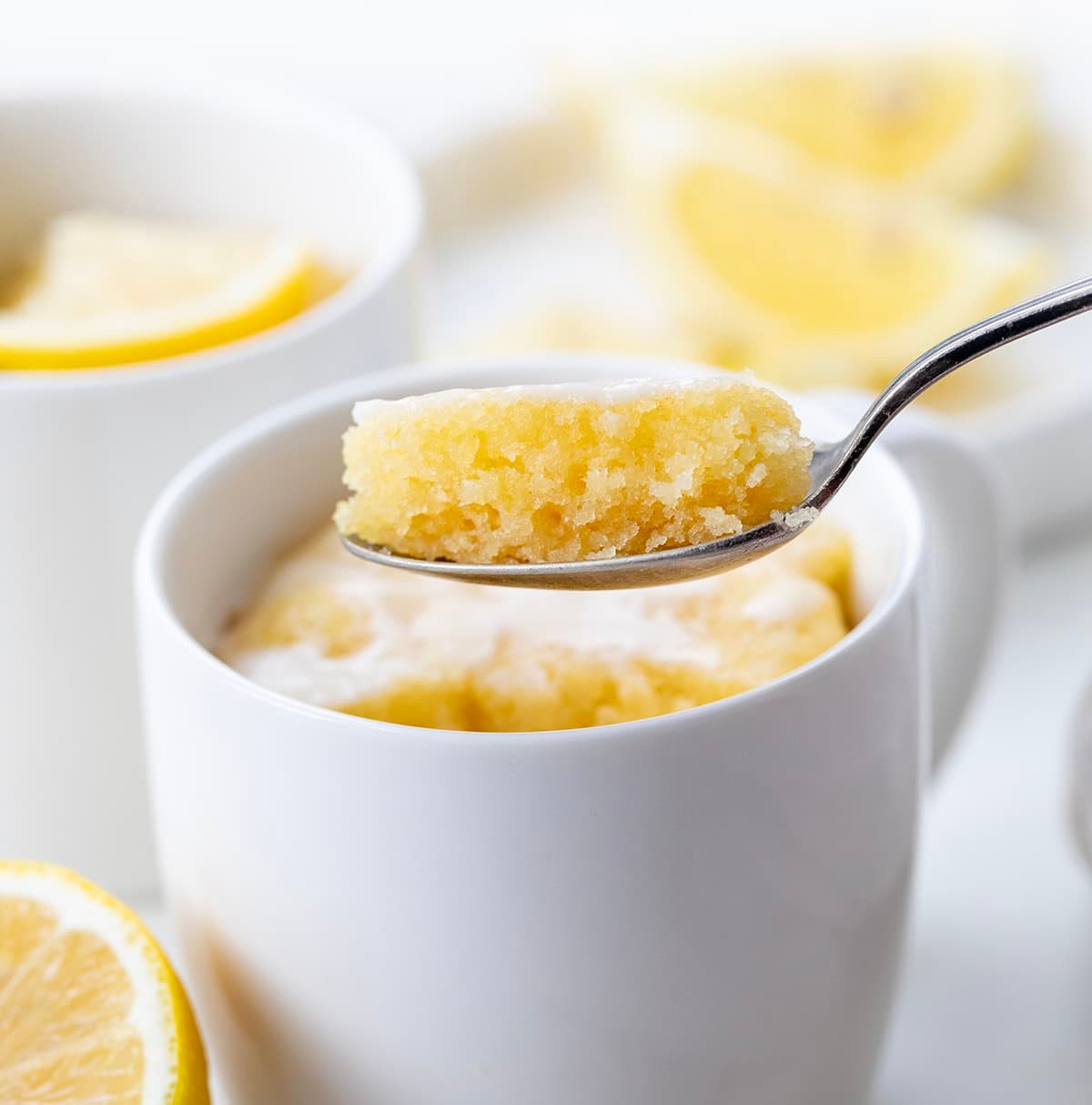 Spoon holding a bite of Lemon Mug Cake directly above the mug.