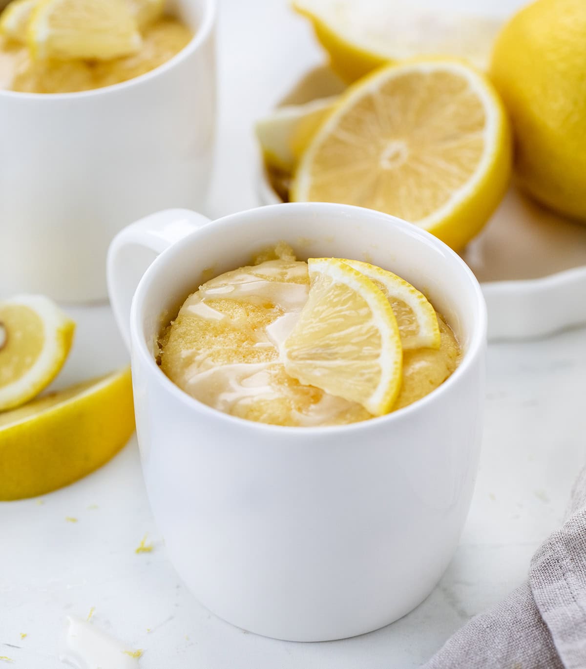 This Lemon Mug Cake is super easy and full of fresh, citrusy flavor. Itโs a quick mug cake recipe you can make in the microwave, perfect when you want a cozy single-serve dessert fast! Soft, sweet, and lemony, this lemon cake totally hits the spot! Lemon Mug Cakes on a white table with fresh lemons.
