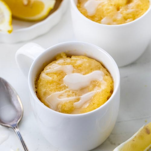 Lemon Mug Cakes in white mugs on a white table from overhead.